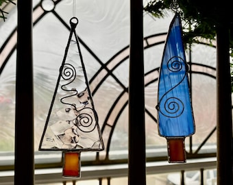 May include: Two hanging stained glass ornaments. One is a clear, textured triangular tree shape with a small orange rectangular base. The other is a blue, elongated, pointed shape with a similar orange base. Both feature decorative silver wire spirals.