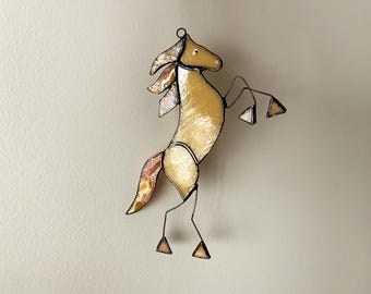 Pode incluir: Estatueta de cavalo em vitral em pose de empinar. O cavalo apresenta um corpo amarelo com aparência texturizada, uma cauda fluida e uma crina com detalhes em rosa e dourado. As pernas são de arame e os cascos triangulares.