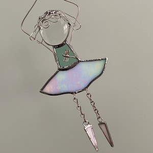 May include: A stained glass figurine of a girl with a clear glass head and a teal bodice with a dragonfly. The skirt is iridescent, and the legs are chains with triangular pendants. The figure is suspended by a wire.