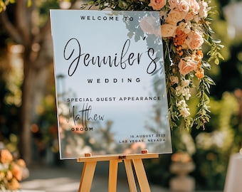 May include: A clear acrylic wedding sign on a wooden easel. The sign reads "Welcome to Jennifer's Wedding" with the names "Matthew, Groom" and the date "16. August. 2025, Las Vegas, Nevada". The sign is decorated with floral arrangements.