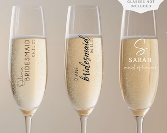 May include: Three clear glass champagne flutes filled with a golden sparkling liquid. Each glass features black vinyl text. The first reads Olivia BRIDESMAID 06.11.25, the second DIANE bridesmaid 06.11.25, and the third S SARAH maid of honour.