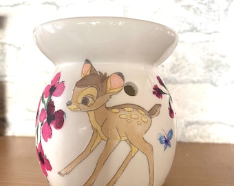 May include: White ceramic wax melt warmer with a cartoon image of Bambi the deer in a forest setting with pink flowers and a blue butterfly.