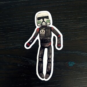 May include: A black and white sticker of a cartoon stormtrooper with a skull and crossbones on its chest. The stormtrooper is wearing a black helmet with a green visor.