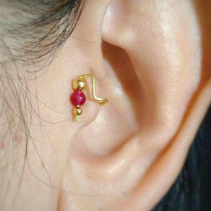 May include: Gold ear cuff with a red gemstone and gold beads. The cuff is worn on the upper part of the ear.