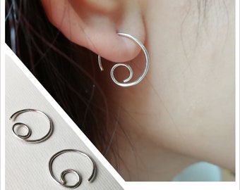 Könnte beinhalten: Silberne Spiral-Creolen. Die Ohrringe bestehen aus einem dünnen Draht, der zu einer Spirale gedreht wird. Die Spirale wird dann zu einem Kreis geformt. Die Ohrringe sind schlicht und elegant.