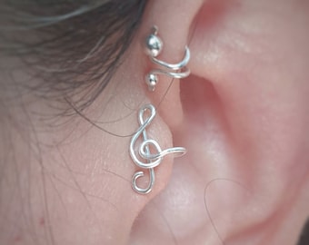 May include: Silver ear cuff with a treble clef design. The cuff is worn on the upper ear, and the treble clef is positioned on the helix.