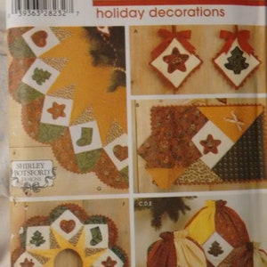 Op de afbeelding: Simplicity Fat Quarter Club vakantiedecoratiepatroon. Het patroon bevat verschillende kerstthema quiltdecoraties, waaronder ornamenten, een tafelloper en cadeauzakjes. De ontwerpen bevatten sterren, harten en kerstbomen.