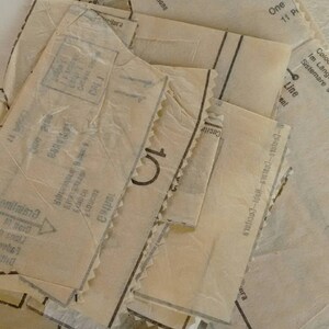 Pu&ograve; includere: Primo piano di una pila di pezzi di cartamodello vintage su uno sfondo di denim blu. I pezzi del cartamodello sono etichettati con istruzioni in pi&ugrave; lingue, tra cui inglese, francese, tedesco, italiano e spagnolo. I pezzi del cartamodello sono per un capo con una linea di posizionamento e un'istruzione di taglio 1.