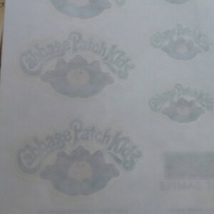 Pu&ograve; includere: Un foglio di carta bianca con quattro adesivi Cabbage Patch Kids. Gli adesivi sono di colore blu chiaro e mostrano il logo Cabbage Patch Kids con una bambola di bambino sorridente.
