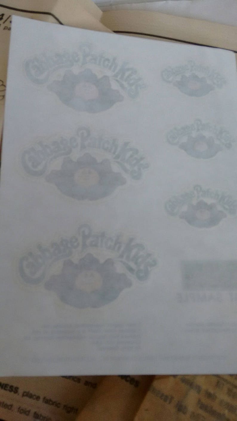 Pu&ograve; includere: Un foglio di carta bianca con quattro adesivi Cabbage Patch Kids. Gli adesivi sono di colore blu chiaro e mostrano il logo Cabbage Patch Kids con una bambola di bambino sorridente.
