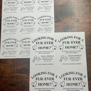 May include: Nine black and white flyers with the text "Looking for a Fur-Ever Home?" and a heart shape with a paw print inside. The flyers also include the text "Let me help with all your real estate needs!" and the name "Megan Smithson" with contact information for "The Realty Group".