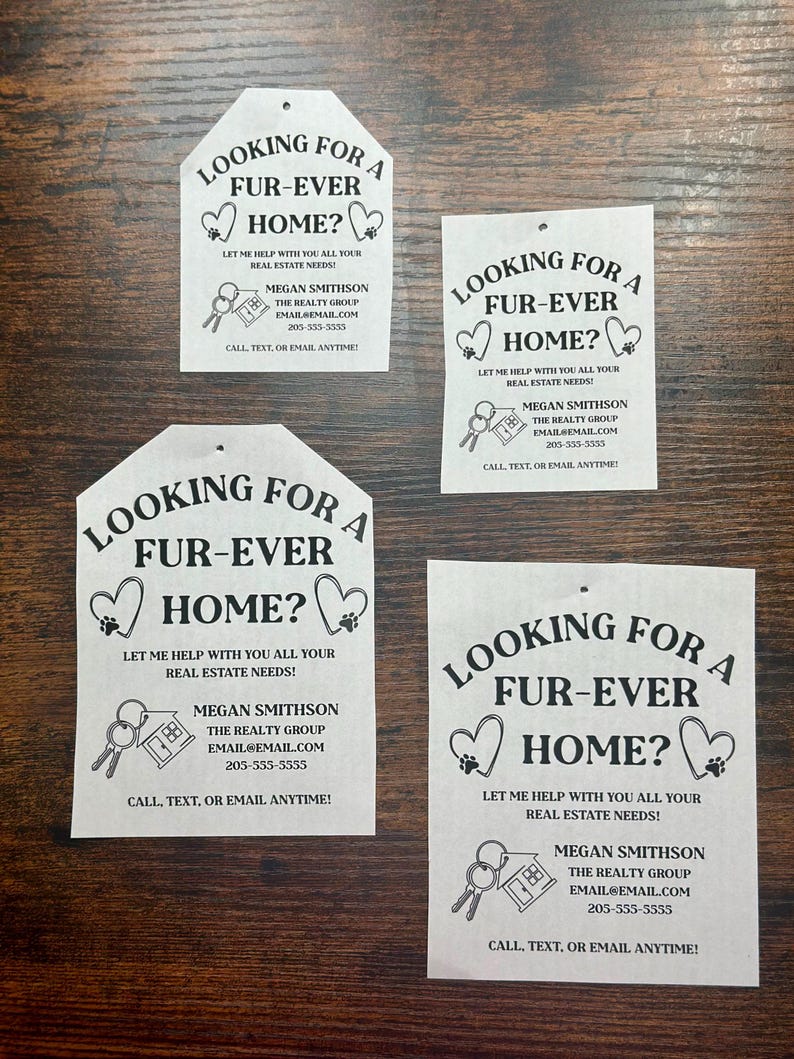 May include: Four white house-shaped signs with black text and graphics. Each sign says "Looking for a Fur-Ever Home?" and includes the text "Let me help with you all your real estate needs!"  The signs also include the name "Megan Smithson", the text "The Realty Group", an email address, and a phone number.  The signs also include a graphic of a key and a house.