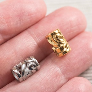 May include: Two metal beads with intricate designs. One bead is gold and the other is silver.