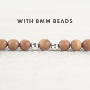May include: Close-up of a wooden beaded bracelet with silver spacer beads. The beads are 8 mm in diameter. "WITH 8MM BEADS" is written above the bracelet.