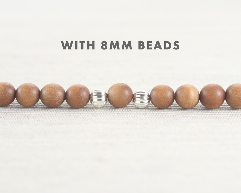 May include: Close-up of a wooden beaded bracelet with silver spacer beads. The beads are 8 mm in diameter. "WITH 8MM BEADS" is written above the bracelet.