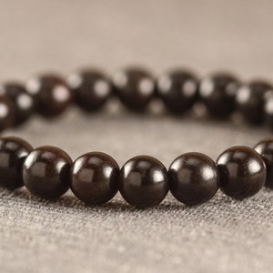 Puede incluir: Un brazalete de cuentas de madera negra con un acabado liso y pulido.