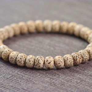 May include: A white beaded bracelet with brown speckles. The beads are round and have a smooth texture.