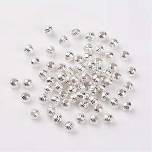 May include: A large pile of silver-colored metal beads with a ridged surface. The beads are round and have a hole in the center.