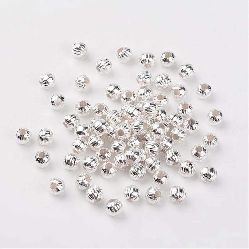 May include: A large pile of silver-colored metal beads with a ridged surface. The beads are round and have a hole in the center.