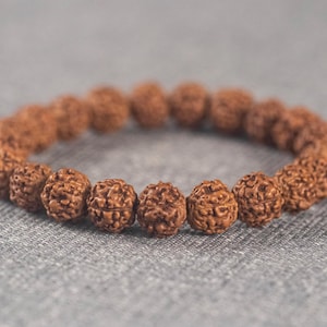 Puede incluir: Un brazalete de madera marrón hecho de cuentas redondas con una superficie texturizada.
