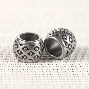 May include: Two silver-colored metal beads with a geometric diamond pattern. The beads are cylindrical with a large central hole and a textured surface. The beads are likely used for jewelry making or crafts.