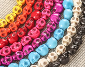 Op de afbeelding: Een kleurrijke streng schedelvormige kralen in verschillende kleuren, waaronder geel, oranje, rood, roze, paars, blauw, wit en zwart.
