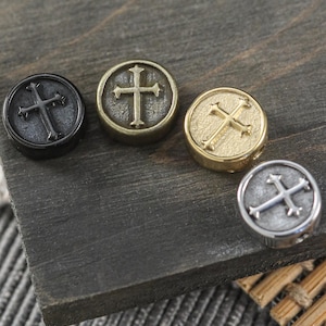May include: Four round metal charms with a cross design. The charms are in black, bronze, gold, and silver.
