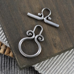 May include: Two silver metal clasps with a decorative swirl design. The clasps are used for jewelry making.