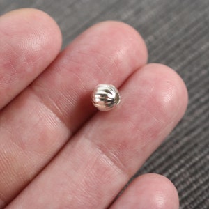May include: A silver bead with a textured, ribbed surface. The bead is round and has a small hole for stringing.