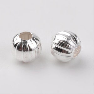 May include: Two silver-toned metal beads with a ribbed design. The beads have a hole in the center for stringing.