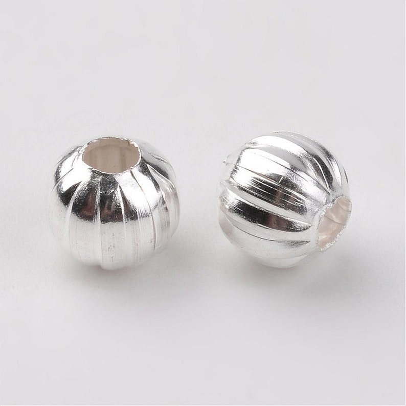 May include: Two silver-toned metal beads with a ribbed design. The beads have a hole in the center for stringing.