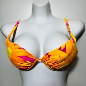 Puede incluir: Un top de bikini de color naranja, amarillo y rosa brillante con estampado floral y tirantes ajustables.
