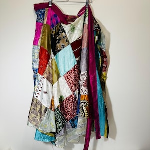 May include: A colorful patchwork wrap skirt made from various fabrics. The skirt features a mix of patterns and colors, including pink, blue, green, and brown. The skirt is tied at the waist and has a long, flowing design.
