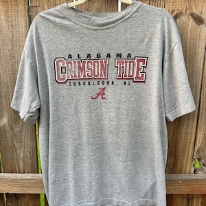 May include: A heather gray short-sleeve t-shirt featuring the text ALABAMA CRIMSON TIDE TUSCALOOSA, AL in maroon and black lettering, with a maroon script letter A logo centered below the text on the front of the garment.