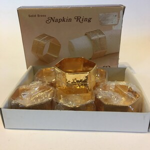 May include: A set of six gold napkin rings in a white box. The box says "Solid Brass Napkin Ring".