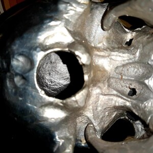 May include: A close-up of a silver skull sculpture with two eye sockets and a detailed, textured surface.