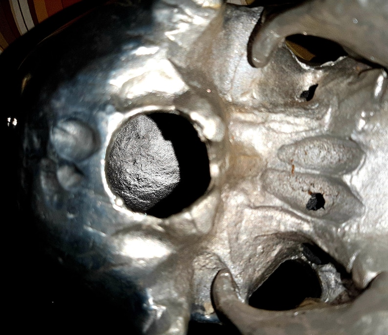 May include: A close-up of a silver skull sculpture with two eye sockets and a detailed, textured surface.