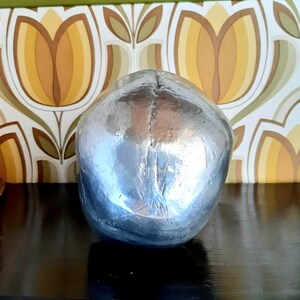 May include: A silver skull sculpture with a smooth, reflective surface. The skull is sitting on a dark surface.