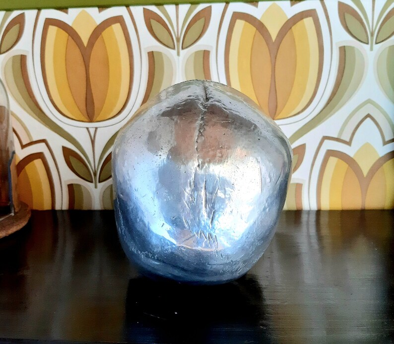 May include: A silver skull sculpture with a smooth, reflective surface. The skull is sitting on a dark surface.