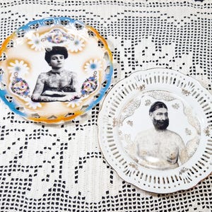 May include: Two decorative porcelain plates. One plate has a blue and orange rim with a portrait of a woman. The other plate is white with a portrait of a man. Both plates have intricate openwork designs.