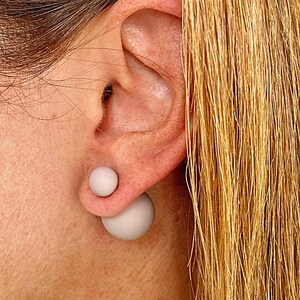 May include: A pair of grey double-sided stud earrings. The earrings are round and have a matte finish.