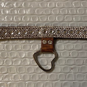 Puede incluir: Un collar de perro de cuero marrón con un dije de corazón plateado y una fila de diamantes de imitación transparentes.