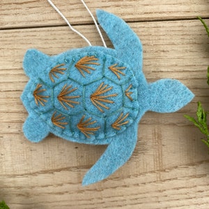 May include: A blue felt sea turtle ornament with a brown embroidered shell pattern. The ornament has a white string for hanging.