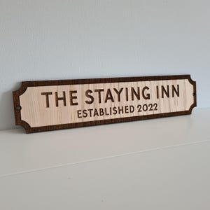 May include: A wooden sign with the text "The Staying Inn Established 2022" in a brown font. The sign has a dark brown border and rounded edges.