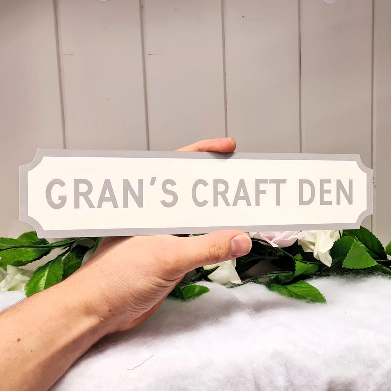 May include: A white sign with gray trim and rounded edges. The sign reads "Gran's Craft Den".