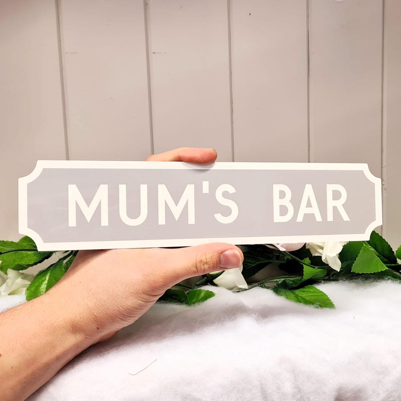 May include: A gray and white sign with the text "MUM'S BAR" in white lettering.