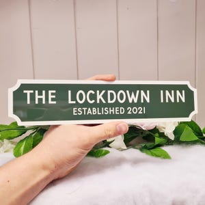 May include: A green and white sign that reads "The Lockdown Inn Established 2021".