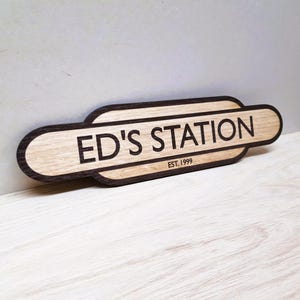 May include: A wooden sign with a dark brown border and a light brown centre. The sign reads "ED'S STATION EST. 1999".