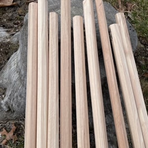 May include: A collection of unfinished wooden dowels, varying in length, arranged on a weathered tree stump. The dowels are a light, natural wood color, showcasing the grain. Ideal for woodworking projects or crafts.