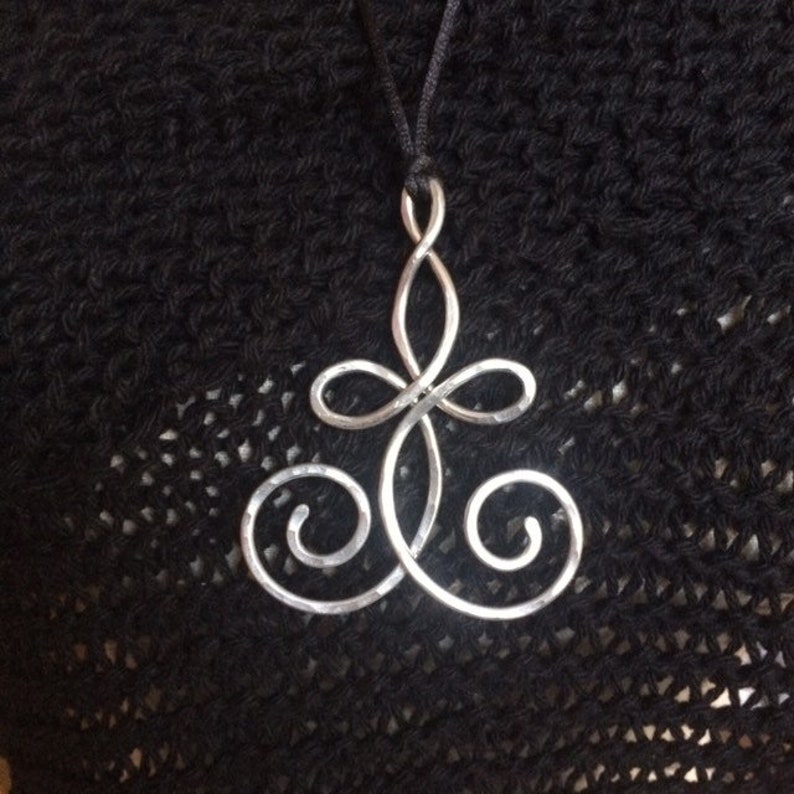 May include: A silver pendant necklace with a swirling, abstract design. The pendant is made of wire and has a hammered texture.